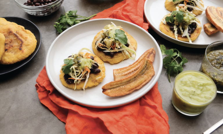 Two Pupusas - a salvadoran street food, made of masa dough and cheese, fried in a ball and topped with black beens and curtido, served on a white plate with a side of plantain chips