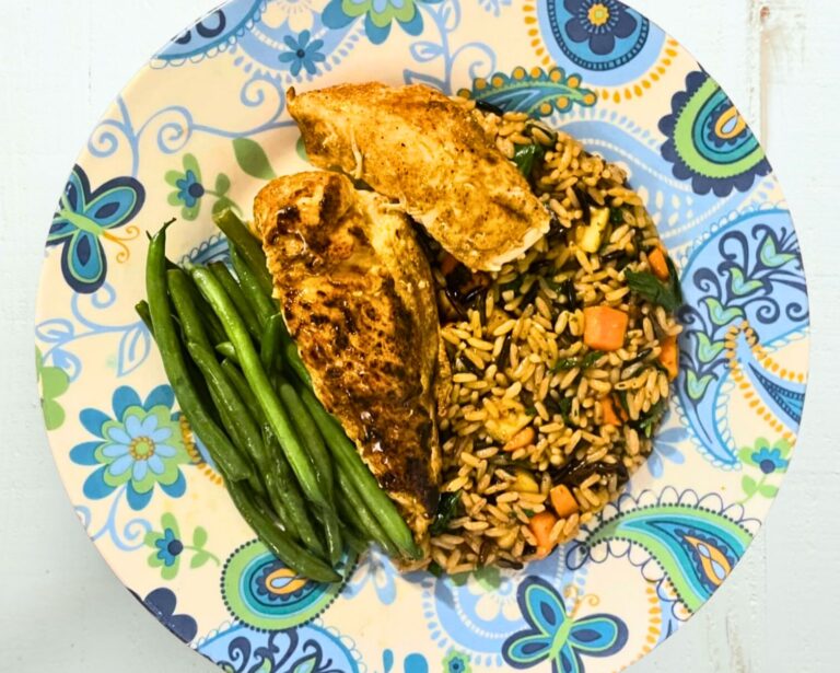 Pan seared chicken breasts with vegetable wild rice and haricot verts served on a white plate with blue filigree
