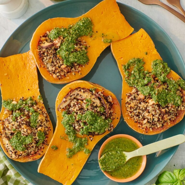 2 butternut squash cut in half lengthwise stuffed with quinoa and shiitake mushrooms, with green chia seed pesto drizzled on top and a bowl of pesto displayed beside, on a blue plate