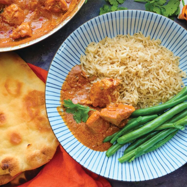 Chicken Tikka Masala served on a blue striped plate with brown rice and haricot vert, naan bread sitting to the side of the plate
