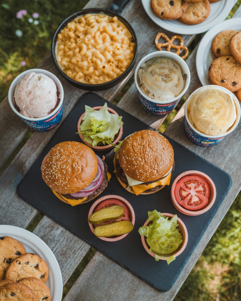 overhead view of a picnic, with two burgers and macaroni and cheese on a wooden picnic table