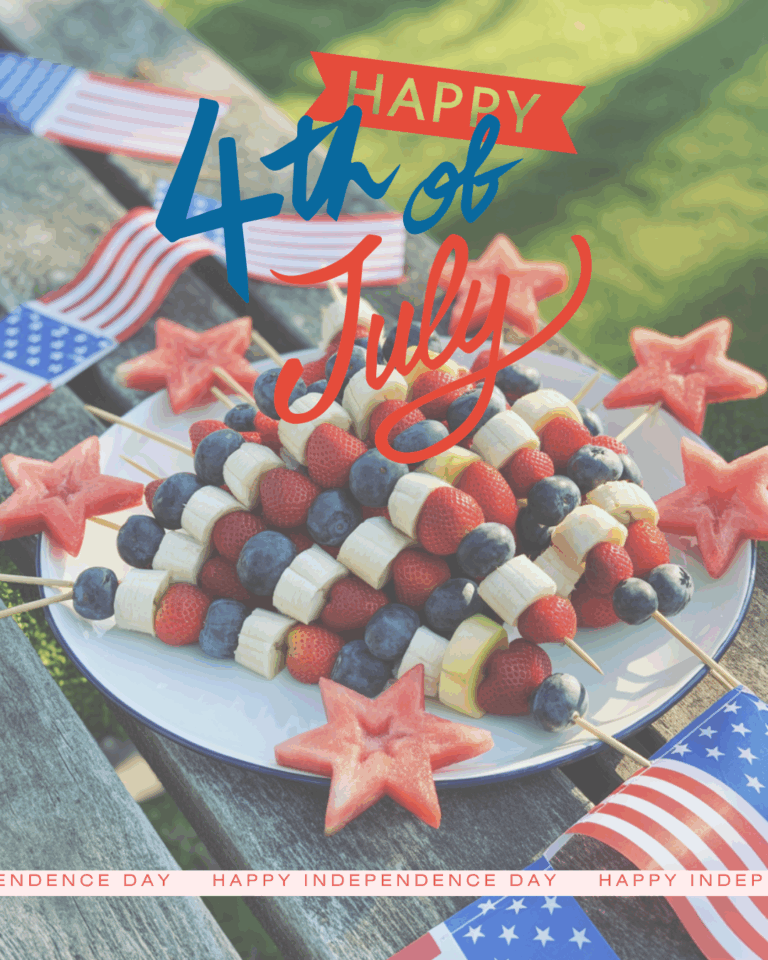 A platter of fresh fruit on a picnic table. The platter has skewers of blueberries, sliced strawberries, and sliced bananas alternating in a red, white, and blue pattern. Each skewer is topped with a watermelon shaped in a star cut-out. The scene is festive, decorated for the fourth of July holiday.